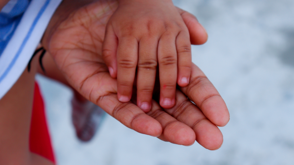 Mão de um bebê em cima da mão de um adulto.
